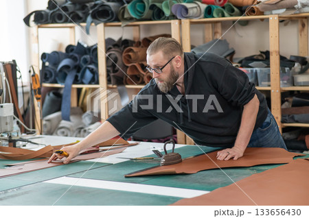 Caucasian bearded man working as a tanner in a workshop. Caucasian bearded man working as a tanner in a workshop. 133656430