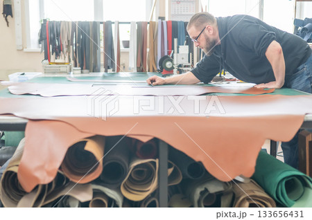 Caucasian bearded man working as a tanner in a workshop. Caucasian bearded man working as a tanner in a workshop. 133656431