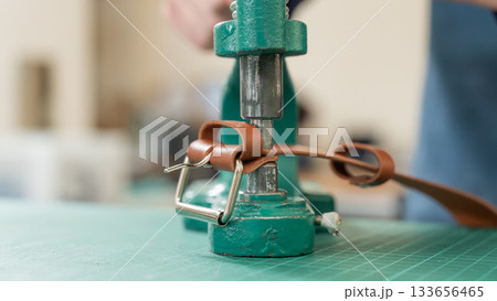 A woman attaches accessories to a leather belt. Leatherworker's workshop. A woman attaches accessories to a leather belt. Leatherworker's workshop. 133656465