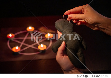 Woman sticking pins into voodoo doll.  133656550