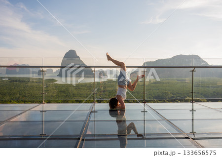Caucasian woman doing forearm stand on glass bridge among mountains.  133656575
