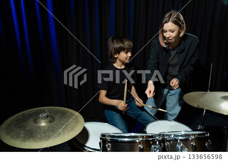 Young caucasian woman teaches a boy to play the drums in the studio on a black background. Music school student 133656598