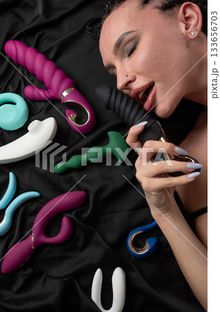 Portrait of Caucasian woman lying on bed among sex toys. Portrait of Caucasian woman lying on bed among sex toys. 133656703