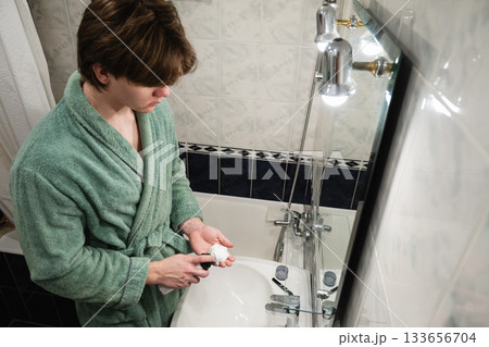 Young man applying shaving cream in bathroom. Morning Shaving Routine Young man applying shaving cream in bathroom. Morning Shaving Routine 133656704
