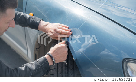 Caucasian man examines and tries to fix a deformation on the body of his car. Caucasian man examines and tries to fix a deformation on the body of his car. 133656722
