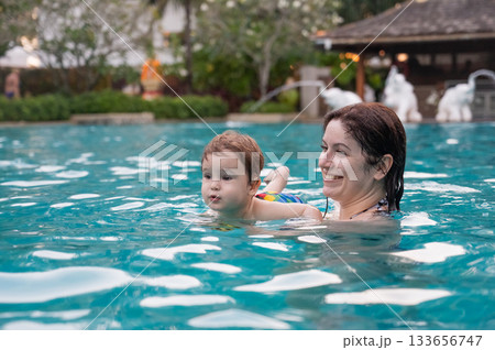 Caucasian woman holds son while swimming in pool on vacation. Caucasian woman holds son while swimming in pool on vacation. 133656747