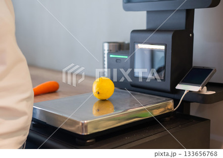 Woman weighing a lemon at a self-checkout. Woman weighing a lemon at a self-checkout. 133656768