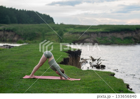 Caucasian woman doing yoga on the river bank. Downward facing dog pose. Caucasian woman doing yoga on the river bank. Downward facing dog pose. 133656840