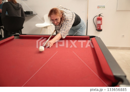 Woman playing pool aiming cue stick at white ball 133656885