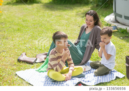 Caucasian woman eats fried sausages with her sons at a picnic. Caucasian woman eats fried sausages with her sons at a picnic. 133656936