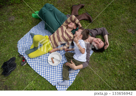 Caucasian woman eats fried sausages with her sons at a picnic.  133656942