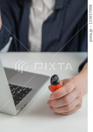 Faceless businesswoman smokes disposable vape and works on laptop.  133657006