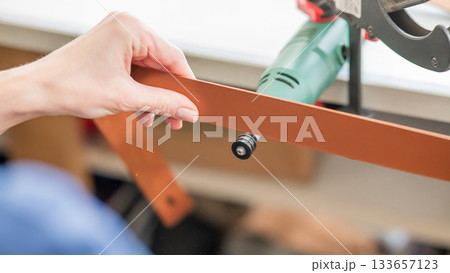 Leatherworker grinding the edge of a strip of leather for a belt in the workshop.  133657123
