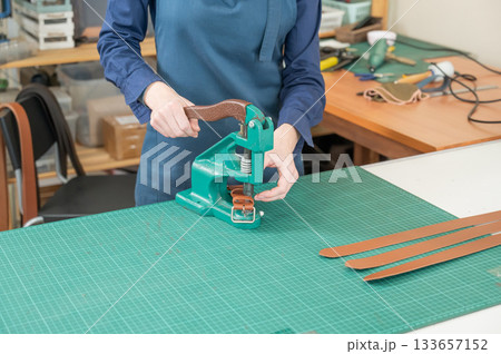 A woman attaches accessories to a leather belt. Leatherworker's workshop.  133657152