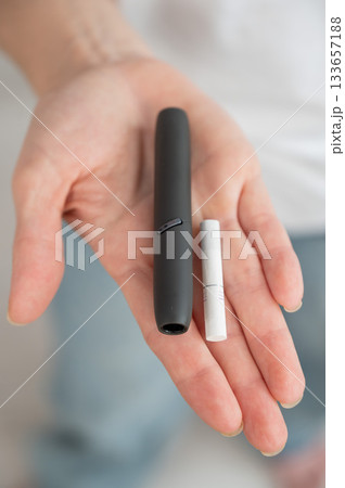 A woman inserts a cigarette stick into a tobacco heating system. Electronic cigarette. A woman inserts a cigarette stick into a tobacco heating system. Electronic cigarette. 133657188