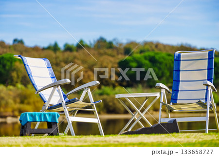 Two empty camp chairs on lake shore 133658727