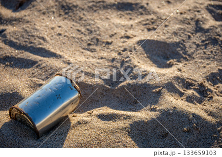 朝の砂浜に落ちた空き缶と環境問題を示す情景 133659103