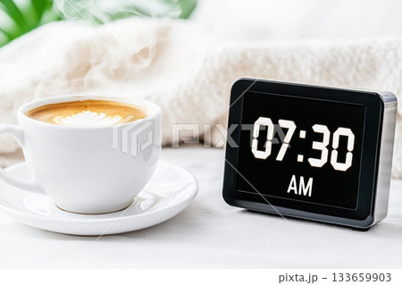 Retro digital flip clock displays 07:30 AM next to a steaming cup of coffee on a minimalist bedside table in a serene morning setting 133659903