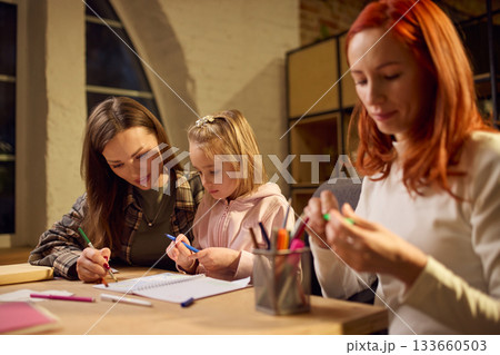 Little girl studying with her mothers in warm evening home setting Little girl studying with her mothers in warm evening home setting 133660503