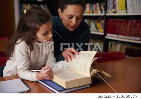 Tutor Helps Child Read In Library During Study Session Tutor Helps Child Read In Library During Study Session 133660577