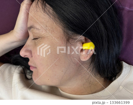 Close up of adult brunette woman sleeping with yellow earplugs, noise protection for healthy sleep, deep rest, insomnia prevention and peaceful home bedroom atmosphere 133661399
