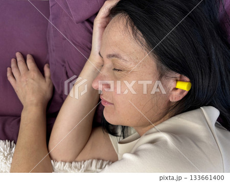 Close up of adult brunette woman sleeping with yellow earplugs, noise protection for healthy sleep, deep rest, insomnia prevention and peaceful home bedroom atmosphere 133661400