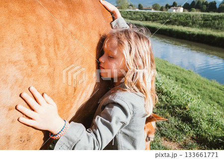 Child Embracing Horse Next to Tranquil Riverbank 133661771