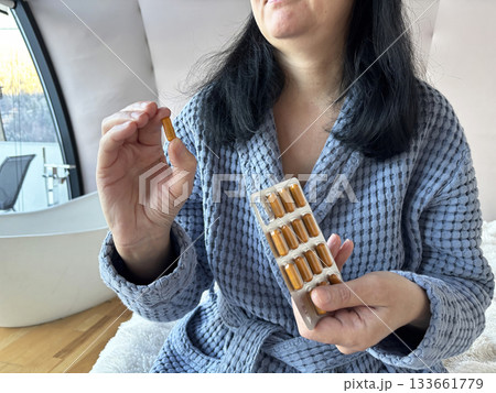 Woman taking vitamins at home, holding a pill and blister pack while following daily healthy lifestyle and immune support routine, home wellness and healthcare concept Woman taking vitamins at home, holding a pill and blister pack while following daily healthy lifestyle and immune support routine, home wellness and healthcare concept 133661779