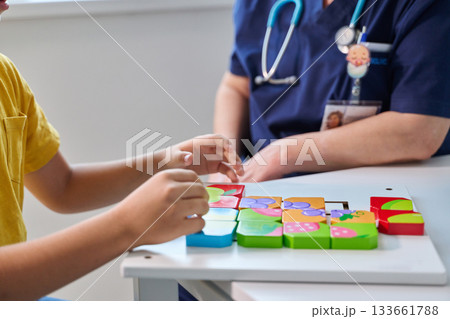 Child engages in playful puzzle activity with healthcare worker in a bright clinic during afternoon hours Child engages in playful puzzle activity with healthcare worker in a bright clinic during afternoon hours 133661788
