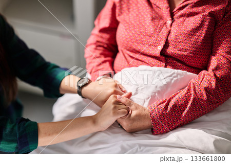Holding hands in a caring moment between generations in a hospital room during the afternoon Holding hands in a caring moment between generations in a hospital room during the afternoon 133661800