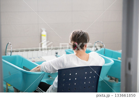 Patient undergoing hydrotherapy treatment with arms immersed in blue rehabilitation tubs inside wellness facility 133661850
