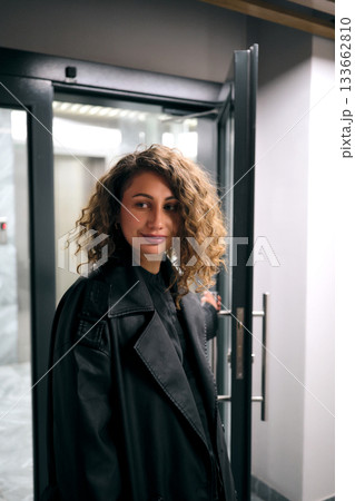 Woman in coat entering modern building smiling Woman in coat entering modern building smiling 133662810