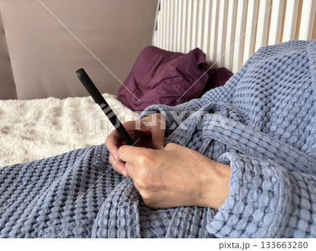 Mature brunette woman with under eye patches working on a smartphone at home, chatting and freelancing while relaxing and combining skincare with remote work 133663280
