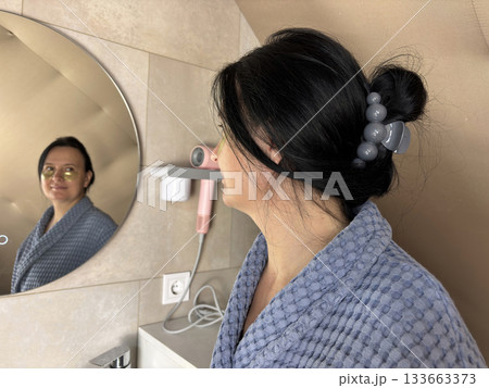 Adult woman in bathrobe standing in front of bathroom mirror applying skincare patches, home beauty routine, rejuvenating facial treatment, wellness and self care concept 133663373