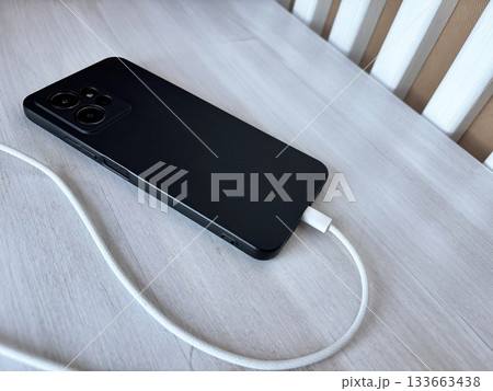 Smartphone charging with a white USB cable, mobile device connected to power adapter, home interior lifestyle, technology usage and daily digital routine concept 133663438