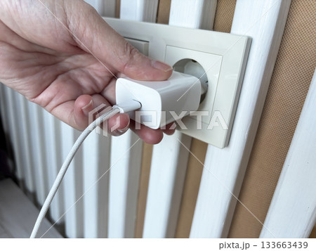 Hand plugging a phone charger into a wall socket, connecting power adapter at home, charging mobile device, everyday technology use and modern lifestyle concept 133663439
