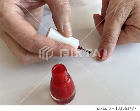 Woman applying red nail polish at home, classic red manicure, self-care beauty routine, close-up of female hands painting nails, nail care and grooming concept 133663477