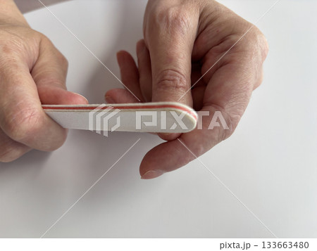 Mature woman filing her nails with a nail file at home, self-care manicure routine, natural nail grooming, beauty and hygiene concept, close up of female hands during home manicure 133663480