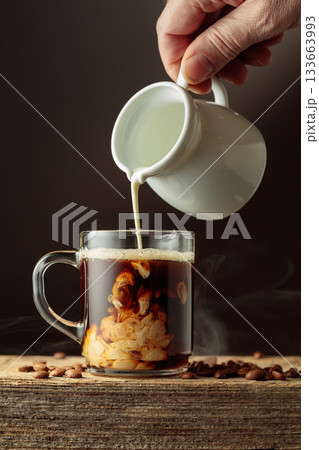 Coffee in a clear glass mug with cream being poured. 133663993