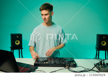 Young DJ with headphones, Skilled DJ engaging with equipment in lively environment, Energetic DJ prepping for live performance amid colorful lighting and fashionable attire Young DJ with headphones, Skilled DJ engaging with equipment in lively environment, Energetic DJ prepping for live performance amid colorful lighting and fashionable attire 133664929