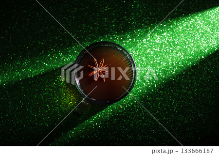 Christmas Holiday Spiced Hot Drink. Glass Cup with Mulled Wine and Star Anise on Glittery Green Background 133666187