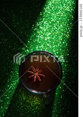 Christmas Holiday Spiced Hot Drink. Glass Cup with Mulled Wine and Star Anise on Glittery Green Background Christmas Holiday Spiced Hot Drink. Glass Cup with Mulled Wine and Star Anise on Glittery Green Background 133666188