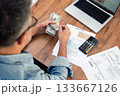 Man calculating utility bills and household expenses with cash and smartphone calculator on wooden desk. Home finance and budget management concept for personal financial planning  133667126