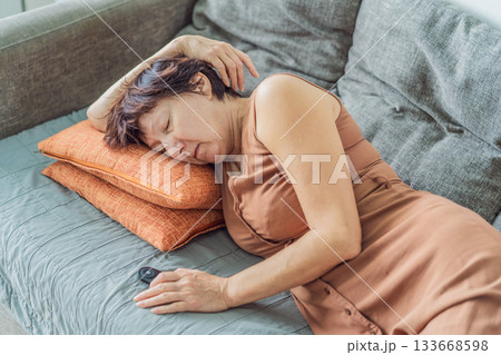 Unaltered senior woman taking a peaceful daytime nap at home, resting comfortably on the sofa in a quiet and cozy environment. Concept of relaxation, wellbeing, healthy aging, slow living and everyday 133668598