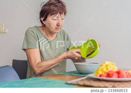 Unaltered senior woman enjoying a calm breakfast at the dining table in a bright home setting. Concept of healthy lifestyle, mindful eating, peaceful morning routine, comfort, wellbeing and everyday Unaltered senior woman enjoying a calm breakfast at the dining table in a bright home setting. Concept of healthy lifestyle, mindful eating, peaceful morning routine, comfort, wellbeing and everyday 133668615