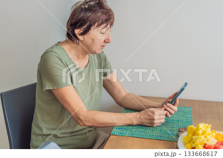 Unaltered senior woman enjoying a calm breakfast at the dining table in a bright home setting. Concept of healthy lifestyle, mindful eating, peaceful morning routine, comfort, wellbeing and everyday 133668617