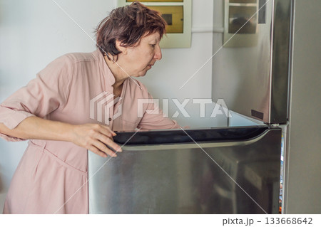 Elderly woman cooking in the kitchen, preparing a homemade meal with care and joy. Concept of healthy aging, independence, domestic life, culinary routine, and active senior lifestyle at home 133668642
