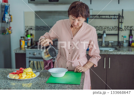 Elderly woman cooking in the kitchen, preparing a homemade meal with care and joy. Concept of healthy aging, independence, domestic life, culinary routine, and active senior lifestyle at home 133668647