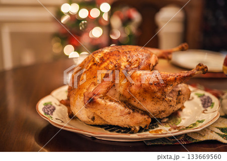 Golden roasted holiday turkey on a festive table with warm Christmas lights in the background, traditional for Christmas and Thanksgiving in the USA. Golden roasted holiday turkey on a festive table with warm Christmas lights in the background, traditional for Christmas and Thanksgiving in the USA. 133669560