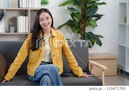 Lifestyle. Smiling young woman in yellow jacket sitting on a couch, radiating positivity. 133671765